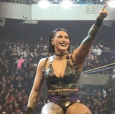 a woman with tattoos on her arm and legs standing in front of a crowd at a wrestling match