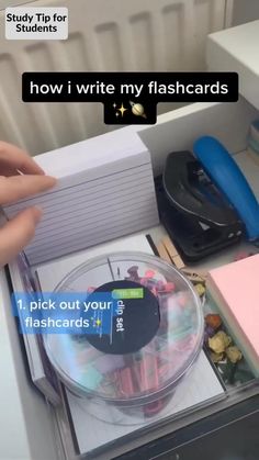 someone is holding their hand over a plastic container filled with pens and other items that are sitting on top of a desk