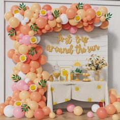 an arch made out of balloons with flowers and sunflowers on the top, in front of a party table