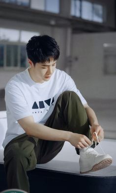 a young man sitting on top of a white bench holding a pair of tennis shoes