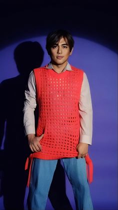 a man standing in front of a purple background wearing a red sweater and blue jeans