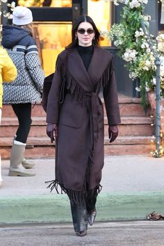 a woman walking down the street wearing a brown coat