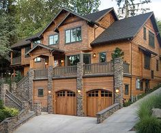 a large wooden house with two garages on the front and second story, surrounded by trees