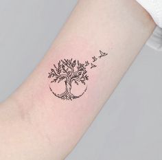 a small tree tattoo on the arm with birds flying around it and an arrow in the middle