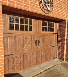 a wooden garage door with an american flag clock on the wall above it and another brick building in the background