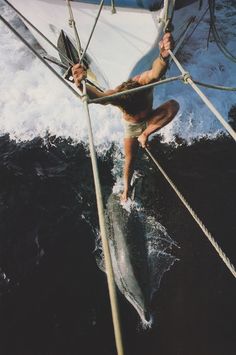 a man riding on top of a boat in the ocean next to a sailboat