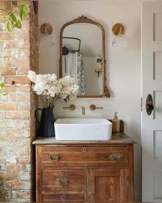 a bathroom sink sitting under a mirror next to a wooden cabinet with flowers in it