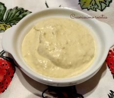 a white bowl filled with cream sauce on top of a floral tablecloth covered table