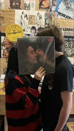 a man and woman kissing each other in front of a wall with posters on it