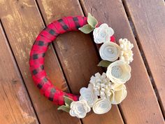 a red and black wreath with white flowers on it sitting on a wooden floor next to a fence