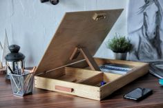 an open wooden box sitting on top of a table next to a cell phone and pen holder