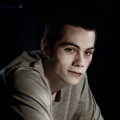 a young man sitting in the dark with his hand on his chest and looking at the camera