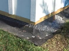 a close up of a metal mesh fence on the side of a building with grass in front of it