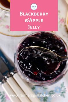 a glass jar filled with blueberry and apple jelly on top of a table next to silverware