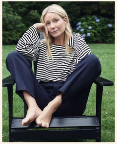 a woman sitting on top of a black bench in the grass with her legs crossed