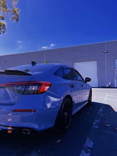 the rear end of a blue car parked in front of a building with a sky background