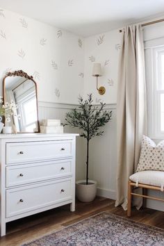 a white dresser sitting next to a window in a room with a rug on the floor