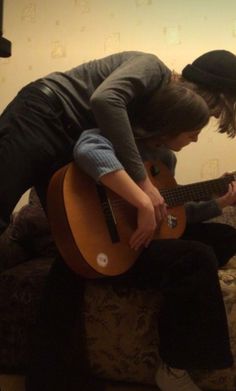 two young men are playing guitars on the couch