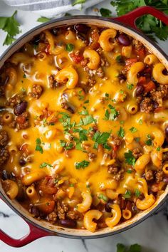 a pot filled with chili macaroni and cheese on top of a table next to cilantro