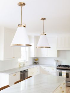 two lights hanging over a kitchen island with marble counter tops and white cabinets in the background