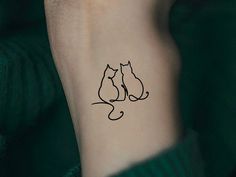 a cat and dog tattoo on the left inner arm, behind a woman's wrist