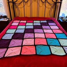 a crocheted granny blanket on top of a bed with red sheets and pillows