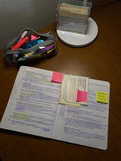 an open notebook with sticky notes and pens on it sitting next to a plastic container