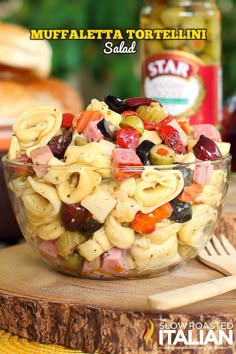 a bowl filled with pasta salad next to a jar of olives and pepperoni