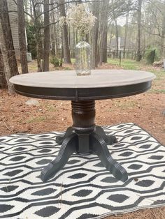 a round table sitting on top of a rug in the middle of a yard with trees