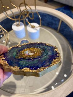 a person holding up a piece of gold and blue agate stone on a glass table