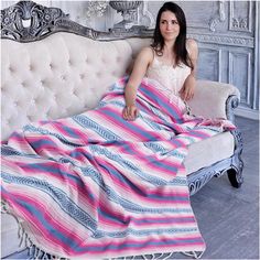 a woman is sitting on a couch with a pink and blue striped blanket over her