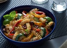 a blue bowl filled with pasta salad on top of a table next to silverware