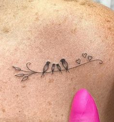 the back of a woman's shoulder with two birds on a branch and hearts