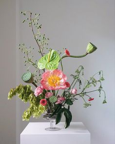 a vase filled with lots of flowers on top of a white table next to a wall