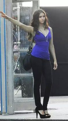 a woman in blue shirt and black pants holding her arm out to the side while walking