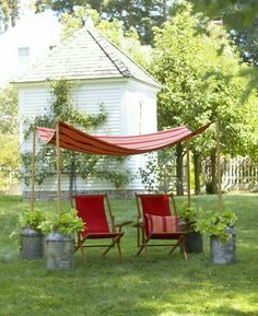 two red chairs sitting in the grass under an awning next to some potted plants