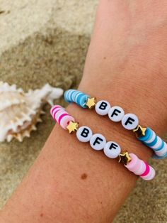 two bracelets with letters and stars on them sitting next to a sea star shell