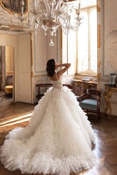 a woman in a white wedding dress is standing near a chandelier