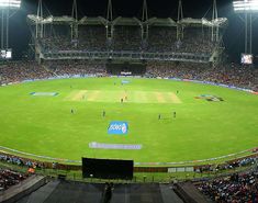 a stadium filled with lots of people watching a cricket game on the field at night