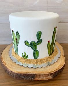 a white cake with green cactus designs on it sitting on a wooden stand next to a wood slice