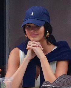 a woman sitting at a table with her hands on her chin wearing a blue hat