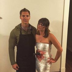 a man standing next to a woman in a silver dress and black apron on top of a hard wood floor