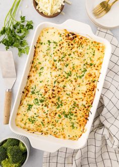 a casserole dish with broccoli, cheese and parsley on the side