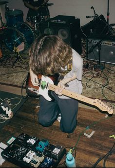 a young man playing an electric guitar on the floor in front of other musical equipment