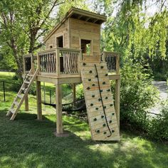 a wooden play structure with a slide and climbing wall in the grass near some trees