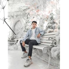 a young man sitting on a bench in front of a snowy tree covered park area