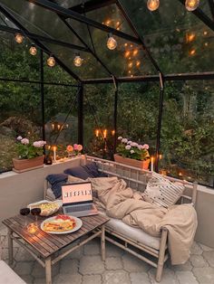 a couch sitting under a glass roof next to a table with food and drinks on it