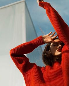 a woman in an orange sweater is holding her hands up to the side while she looks off into the distance