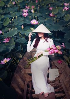 a woman sitting on top of a wooden boat filled with water lillies and holding flowers