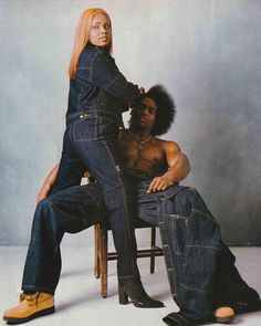 a man sitting next to a woman on top of a chair in front of a gray background